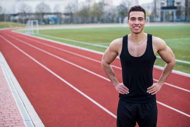 Retrato de un sonriente joven atleta masculino de pie en la pista de carreras