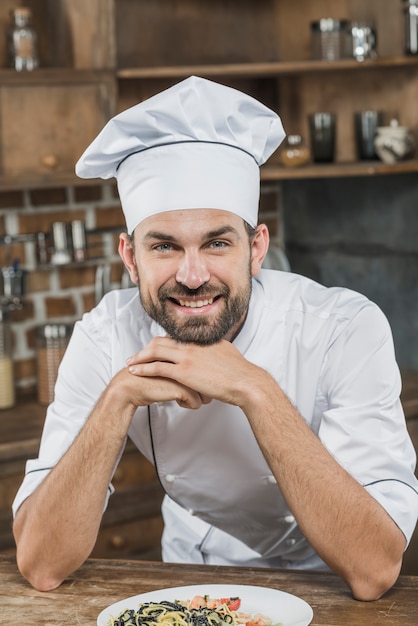 Foto gratuita retrato de sonriente joven chef masculino profesional con su plato preparado