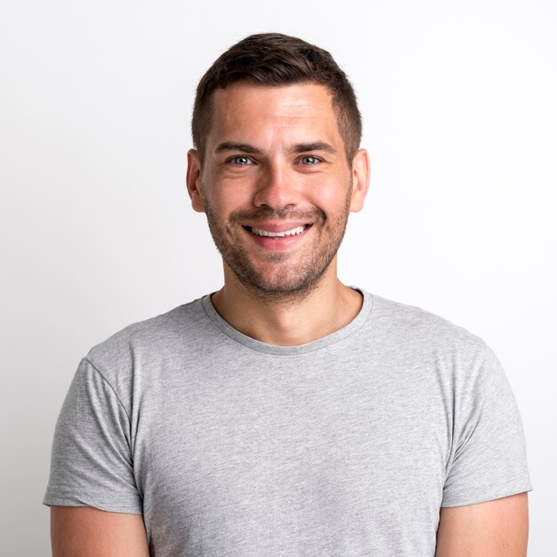 Retrato de sonriente joven encantador en camiseta gris de pie contra el fondo liso