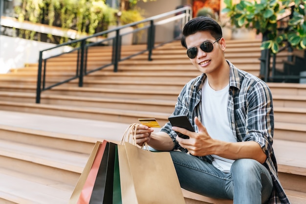 Retrato sonriente joven guapo en gafas de sol con bolsa de papel