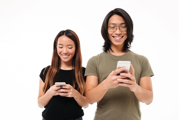 Retrato de una sonriente joven pareja asiática utilizando teléfonos móviles