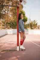 Foto gratuita retrato sonriente de una joven patinadora de pie junto a la portería de fútbol