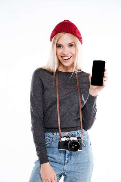 Retrato de una sonriente joven rubia fotógrafo mostrando teléfono móvil