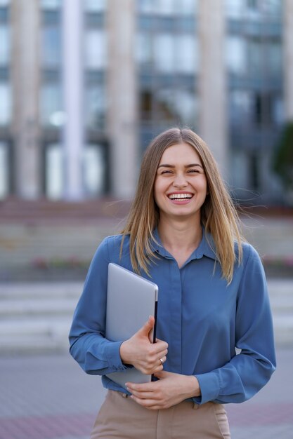 Retrato sonriente joven rubia vistiendo la camiseta azul suave sobre edificio