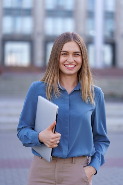 Retrato sonriente joven rubia vistiendo la camiseta azul suave sobre edificio