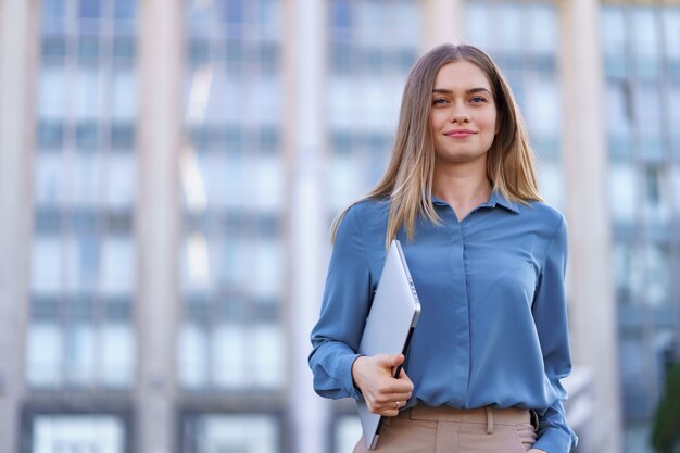 Retrato sonriente joven rubia vistiendo la camiseta azul suave sobre edificio