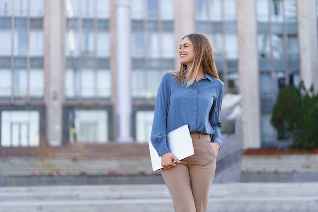 Retrato sonriente joven rubia vistiendo la camiseta azul suave sobre edificio