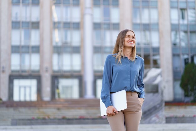 Retrato sonriente joven rubia vistiendo la camiseta azul suave sobre edificio