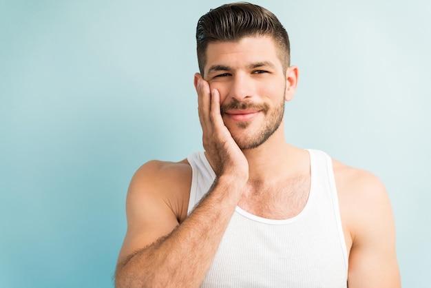 retrato, de, sonriente, macho joven, con, entregue, mejilla, llevando, blanco, chaleco, contra, plano de fondo