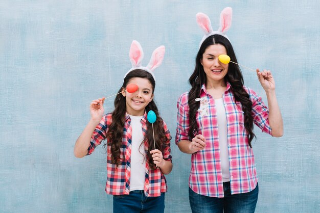 Retrato sonriente de una madre y una hija que cubren un ojo con el apoyo del huevo de Pascua