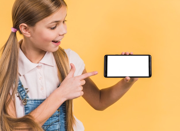 Retrato sonriente de una muchacha con el pelo rubio largo que señala en el teléfono móvil que muestra la pantalla en blanco blanca