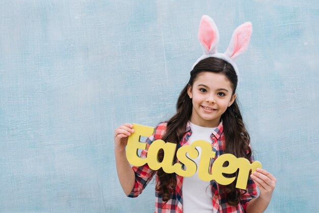 Retrato sonriente de una muchacha que lleva a cabo la palabra amarilla de pascua que mira a la cámara