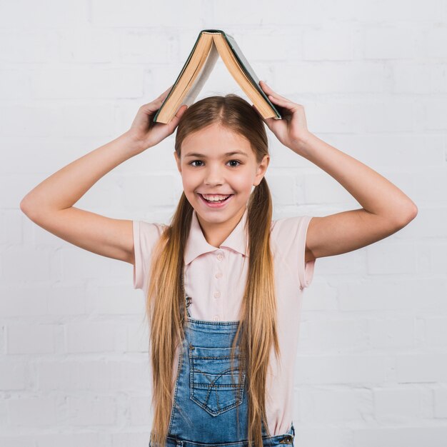 Retrato sonriente de una muchacha que sostiene un libro abierto en su cabeza que mira a la cámara