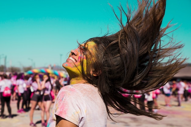 Retrato sonriente de una mujer joven con color holi sacudiendo su cabello