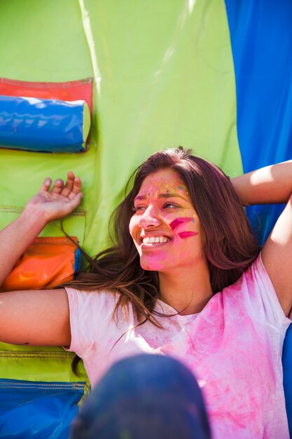 Retrato sonriente de una mujer joven con color del holi en su cara que mira lejos