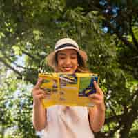 Foto gratuita retrato sonriente de la mujer joven que se coloca en el mapa de la lectura del parque