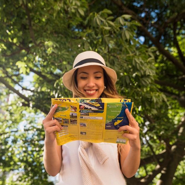 Retrato sonriente de la mujer joven que se coloca en el mapa de la lectura del parque