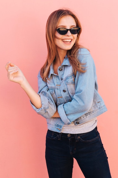 Retrato sonriente de una mujer joven que llevan las gafas de sol contra el contexto rosado