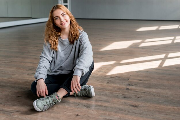 Retrato sonriente de una mujer joven que se relaja en el piso de madera dura en el estudio de la danza