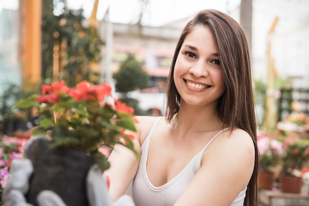 Retrato sonriente de una mujer joven que sostiene la planta floreciente