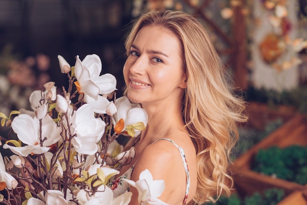 Retrato sonriente de una mujer joven rubia con las flores hermosas blancas