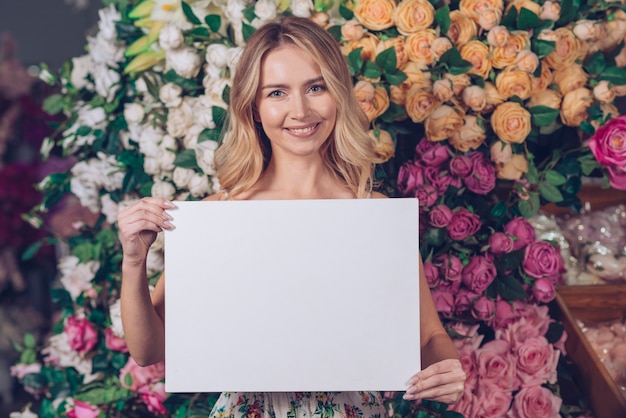 Foto gratuita retrato sonriente de una mujer joven rubia que muestra la tarjeta blanca en blanco