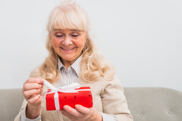 Retrato sonriente de una mujer mayor rubia que abre la caja de regalo roja