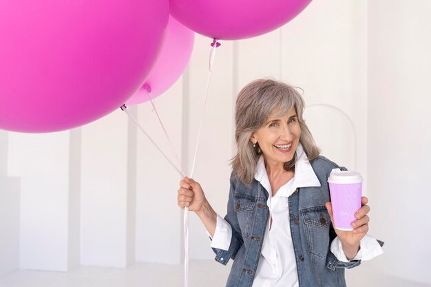 Retrato, de, sonriente, mujer mayor, tenencia, taza, y, rosa, globos