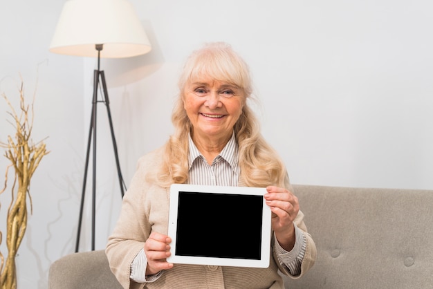 Retrato sonriente de una mujer senior mostrando tableta digital con pantalla en blanco