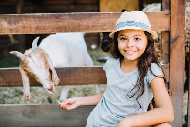 Retrato sonriente de una niña alimentando a la cabra en el establo