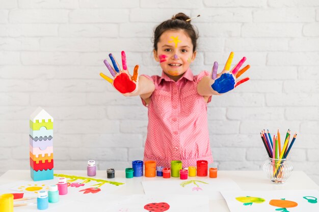 Retrato sonriente de una niña que muestra su mano pintada de colores a la cámara