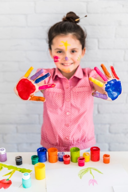 Retrato sonriente de una niña que muestra su mano pintada de colores