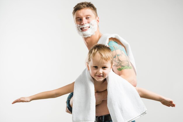 Retrato sonriente de padre con espuma de afeitar en sus mejillas jugando con su hijo