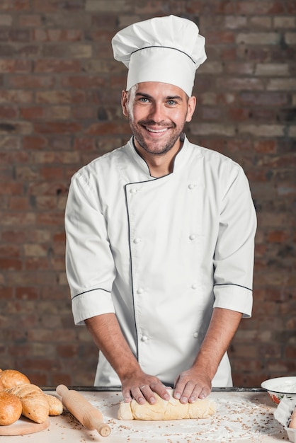 Retrato de sonriente panadero masculino amasando la masa