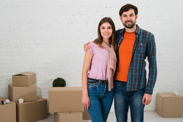 Retrato sonriente de una pareja joven con cajas de cartón en su nueva casa