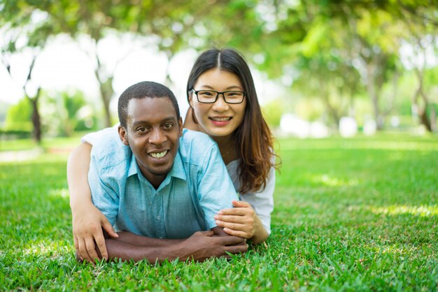 Retrato de sonriente pareja multiétnica tumbado en la hierba en el parque