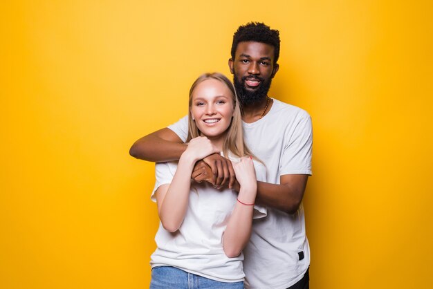 Retrato de sonriente pareja de raza mixta posando sobre pared amarilla en estudio y mirando al frente