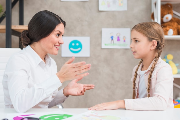 Retrato sonriente de una psicóloga y una niña que tiene una conversación en la oficina