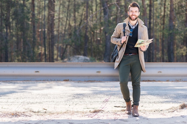 Foto gratuita retrato sonriente de un viajero masculino que sostiene su mochila y mapa