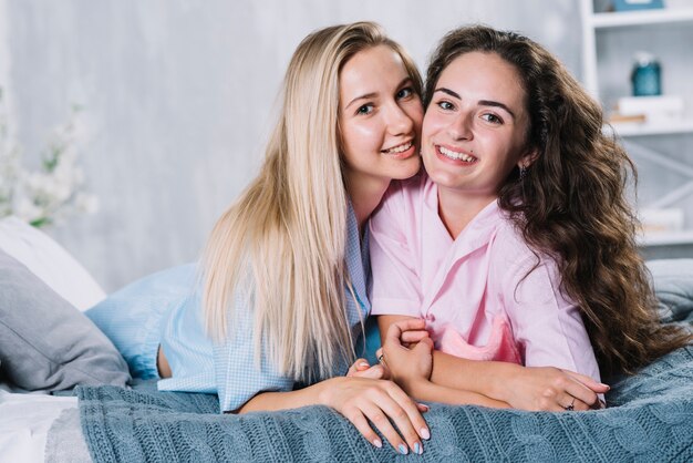 Retrato de sonrientes jóvenes amigas acostado en la cama