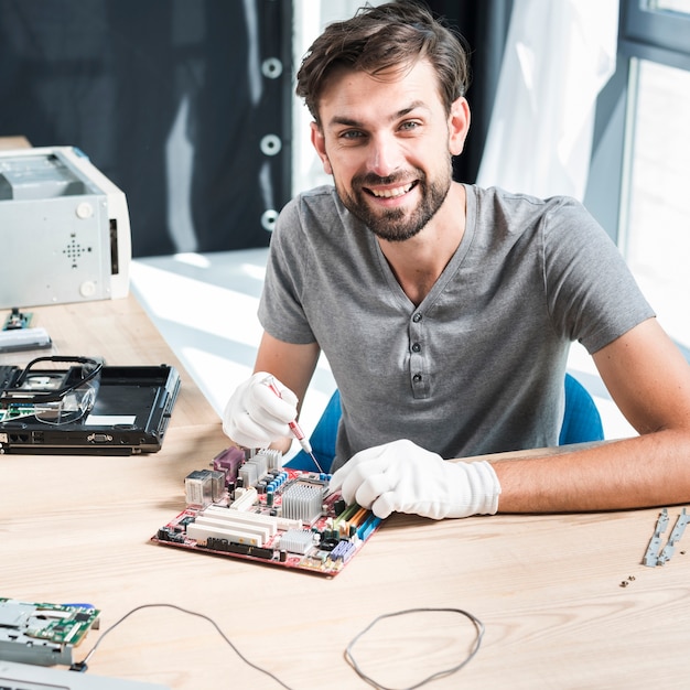 Foto gratuita retrato de un técnico de sexo masculino sonriente que repara la placa madre del ordenador