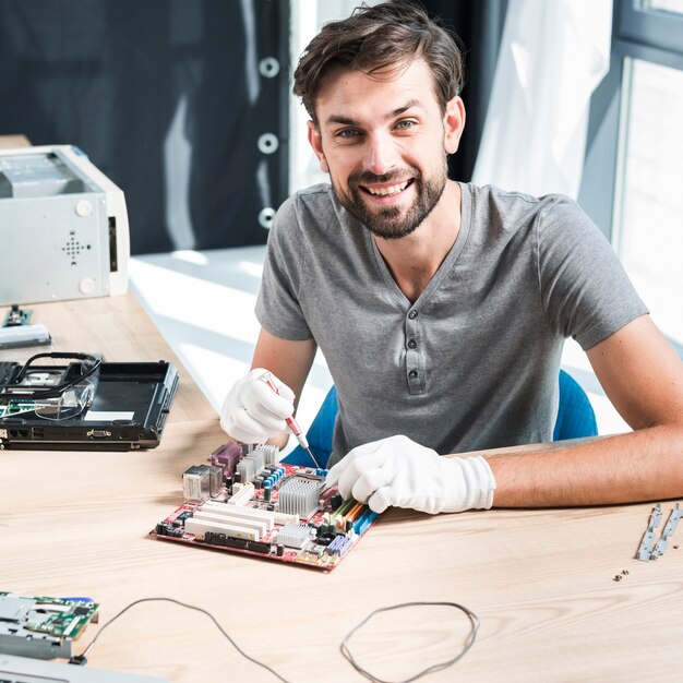 Retrato de un técnico de sexo masculino sonriente que repara la placa madre del ordenador