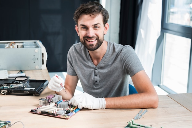 Retrato de un técnico de sexo masculino sonriente que trabaja en la placa madre del ordenador