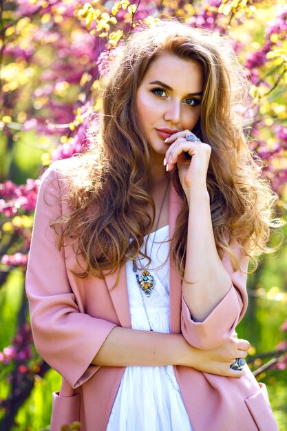 Retrato de tendencias de primavera de elegante magnífica mujer con estilo hermosa posando cerca de árboles florecientes en el jardín de la ciudad