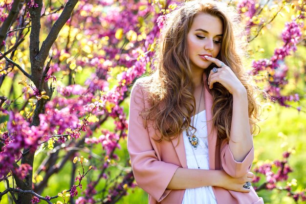 Retrato de tendencias de primavera de elegante magnífica mujer con estilo hermosa posando cerca de árboles florecientes en el jardín de la ciudad