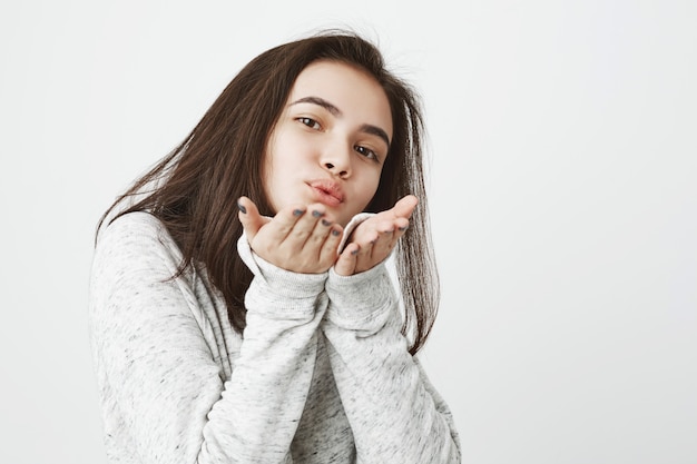 Retrato de tierna joven encantadora enviando besos y mostrándolo con gesto