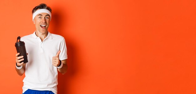 Retrato de un tipo de fitness saludable y activo de mediana edad con uniforme de gimnasio que muestra el pulgar hacia arriba bebiendo