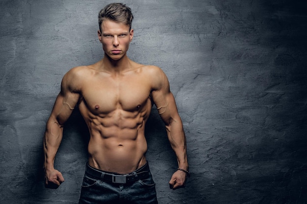 Retrato de un tipo musculoso fuerte sin camisa sobre fondo gris.