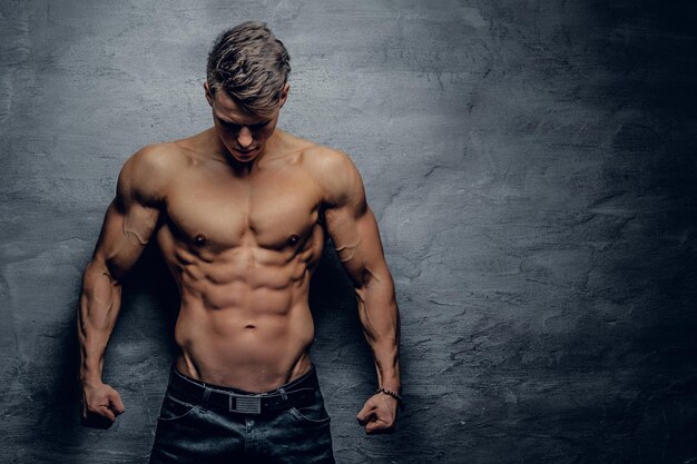 Retrato de un tipo musculoso fuerte sin camisa sobre fondo gris.