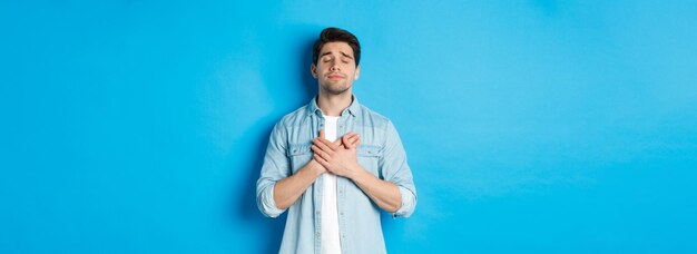 Retrato de un tipo soñador y nostálgico vestido con ropa informal cogidos de la mano en el corazón y ojos cerrados soñar despierto